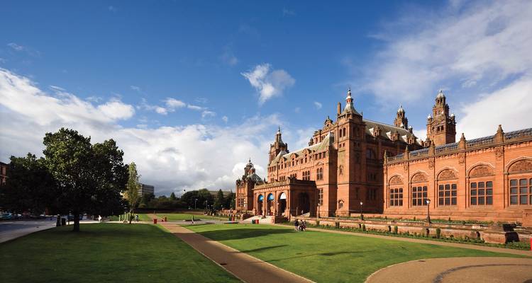 Gran Galería de Arte y Museo Kelvingrove de arenisca roja con amplios jardines bajo un cielo brillante.