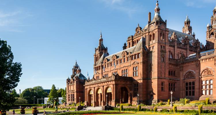 Rotes Sandstein-Kelvingrove Art Gallery and Museum in hellem Sonnenschein mit Besuchern, die sich auf dem Rasen entspannen.