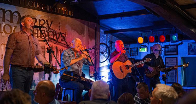 Músicos tradicionales interpretan música folclórica animada en el escenario dentro de un acogedor pub irlandés.