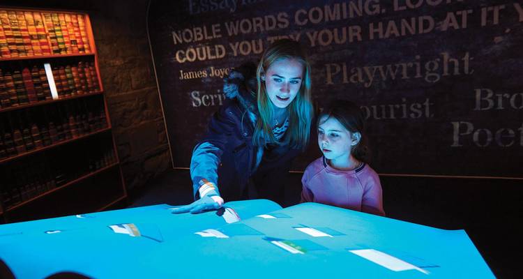 Adult and child interact with illuminated displays inside a literary museum exhibit.