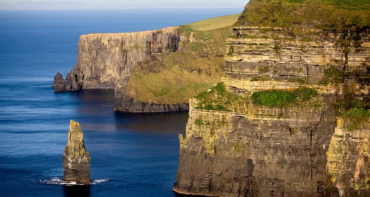 Close-up view of towering sea cliffs and solitary sea stack rising from deep blue waters.