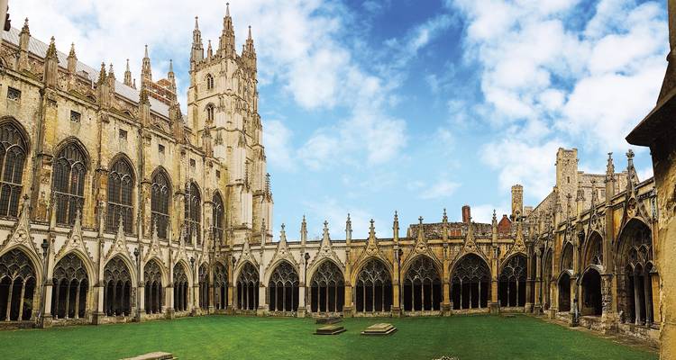 Cour du cloître de la cathédrale de Canterbury entourée d'arcs gothiques et de flèche contre le ciel bleu.