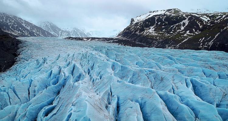 Vaste glacier bleu avec des crevasses spectaculaires s'étendant vers des montagnes enneigées.
