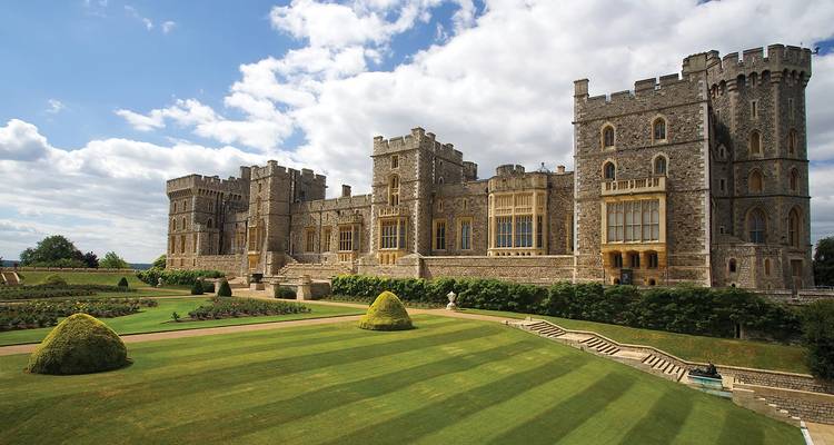 Vue panoramique de la façade majestueuse du château de Windsor et de ses pelouses parfaitement rayées sous un ciel lumineux.