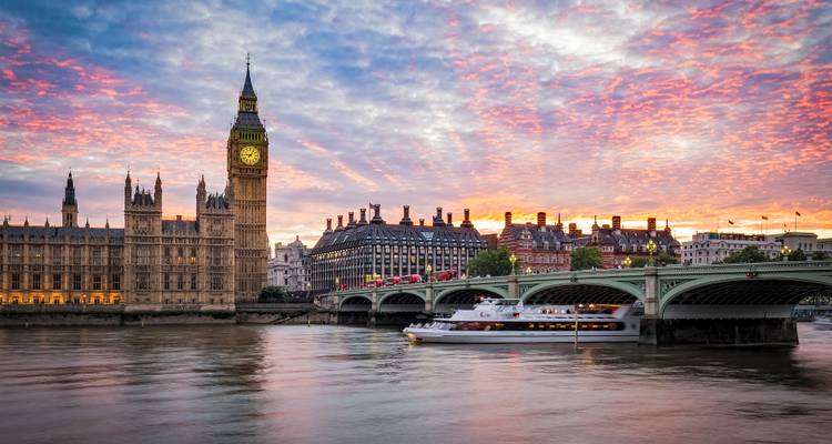L'emblématique Big Ben et les Chambres du Parlement au bord de la Tamise au coucher du soleil éclatant, avec un bateau de croisière passant sous le pont de Westminster.