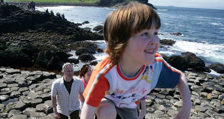 Family explores the Giant's Causeway basalt columns with child climbing in the foreground.