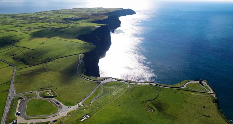 Sun-drenched aerial silhouette of the Cliffs of Moher jutting into the Atlantic with sparkling sea.