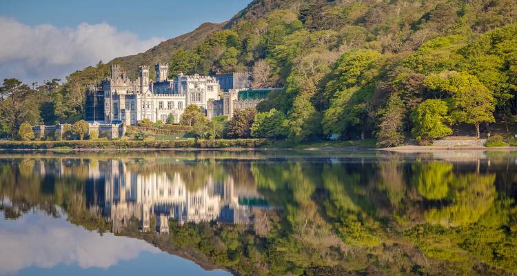 Kylemore Abbey reflects on a still lake surrounded by dense spring foliage and mountain backdrop.