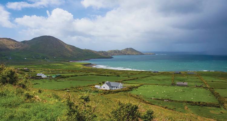Coastal farmland with patchwork fields, cottages and turquoise bay framed by gentle hills.