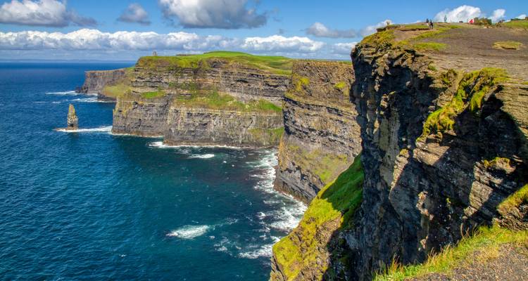 Iconic Cliffs of Moher plunging into deep blue Atlantic waters under scattered clouds.