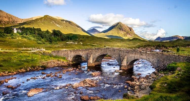 Steinerne gewölbte Sligachan-Brücke, die einen lebhaften Fluss überspannt, mit den schroffen Cuillin-Bergen im Hintergrund.