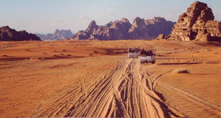 Les véhicules tout-terrain laissent des traces parallèles à travers les vastes sables orange du désert de Wadi Rum avec des montagnes escarpées à l'horizon.