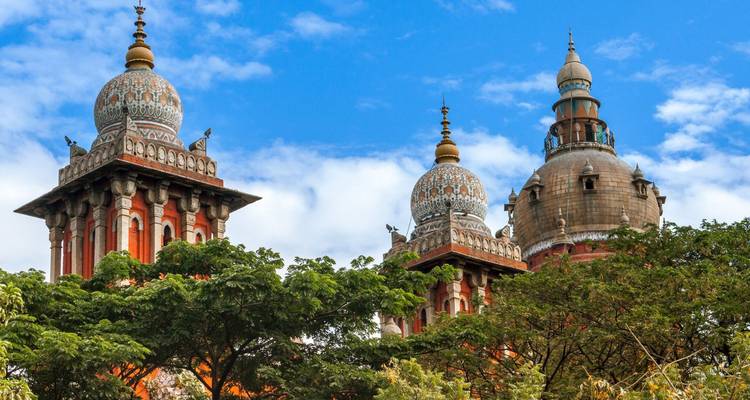 Verzierte Kuppeln des historischen Obersten Gerichtsgebäudes, die sich über üppige Bäume vor einem blauen Himmel in Chennai erheben.