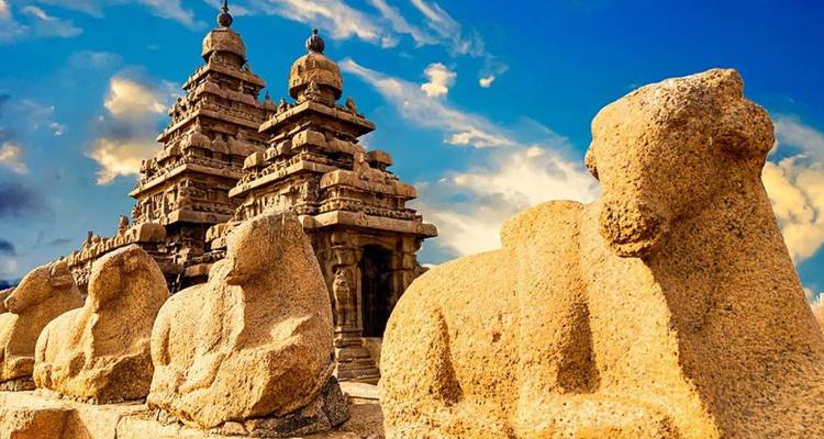 Sonnenbeschienener Ufer-Tempel mit Granit-Nandi-Stieren im Vordergrund unter dramatischem Abendhimmel in Mahabalipuram.