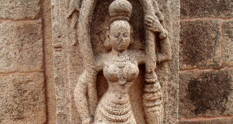 Nahaufnahme einer antiken Steingöttinnenskulptur mit verwitterter Textur an einer Tempelwand.