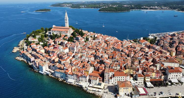 Panorama aérien de la péninsule de la vieille ville de Rovinj avec le clocher en pierre de l'église entouré par les eaux bleu profond de la mer Adriatique.