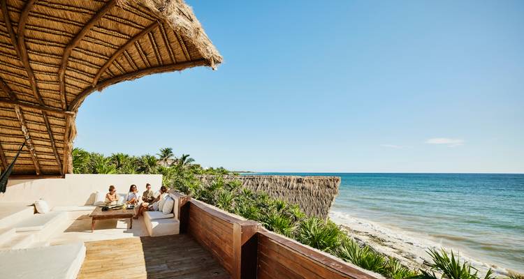 Des amis se détendent sur une terrasse ombragée en bord de mer avec vue sur l'océan turquoise.