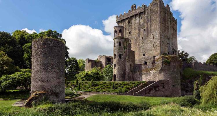 Château de Blarney en pierre médiévale s'élevant au milieu d'une verdure luxuriante sous un ciel irlandais d'un bleu éclatant