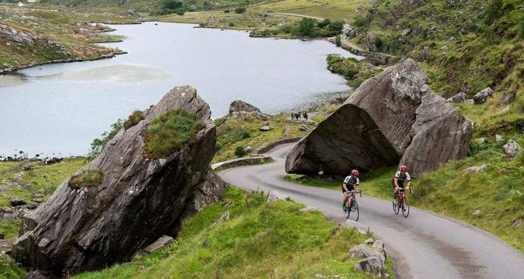 Deux cyclistes pédalant sur une route étroite et sinueuse passant devant des rochers spectaculaires au bord d'un lac serein dans l'Anneau du Kerry