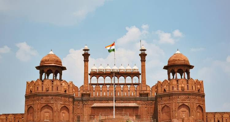 Vorderfassade von Delhis Rotem Fort, gekrönt von der indischen Trikolore-Flagge vor blauem Himmel.