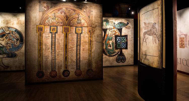 Sala de exposición con iluminación tenue que muestra páginas ornamentadas de manuscritos medievales e ilustraciones.