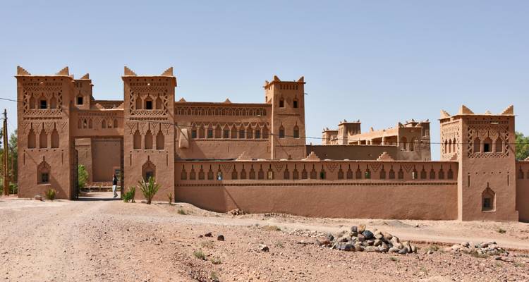 Große Adobe-Kasbah-Festung mit dekorativen Türmen steht gegen klaren Himmel in trockener Landschaft.