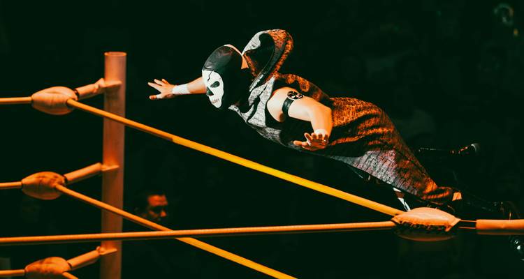Lutteur de lucha libre masqué volant par-dessus les cordes à l'intérieur d'un ring de catch vivement éclairé pendant un match.