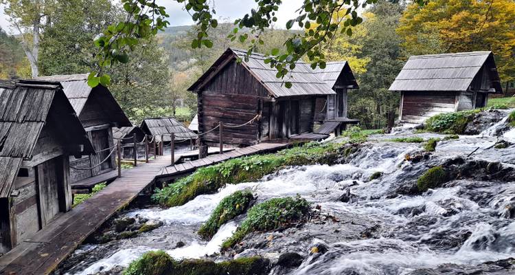 Alte hölzerne Wassermühlen, verbunden durch schmale Stege neben einem reißenden Bach in einem bewaldeten Tal