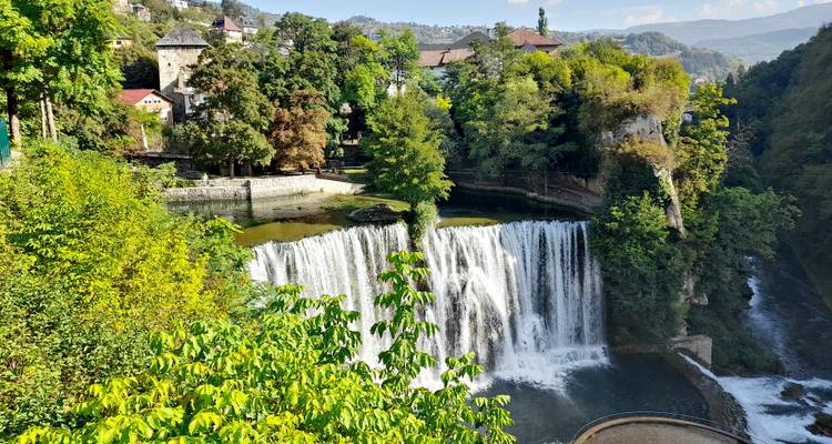 Mächtiger Wasserfall, der unter einer historischen Bergfestung herabstürzt, umgeben von dichtem Grün