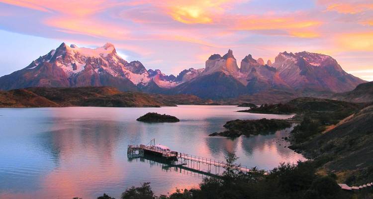 Coucher de soleil pastel sur le lac Pehoé avec les pics des Torres del Paine et une petite jetée au premier plan.