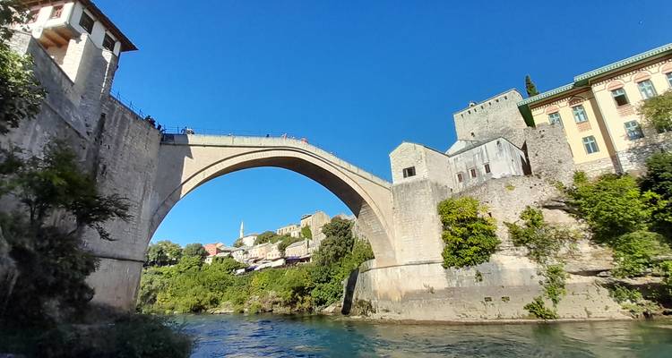 Icónico puente de arco de piedra Stari Most que cruza el río Neretva bajo un cielo azul despejado.