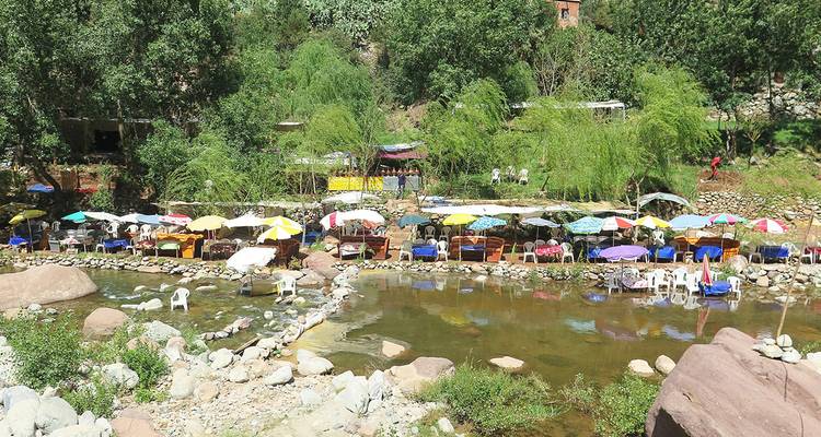 Tables and colourful umbrellas are set directly in a shallow river creating a unique outdoor dining scene in a leafy valley.