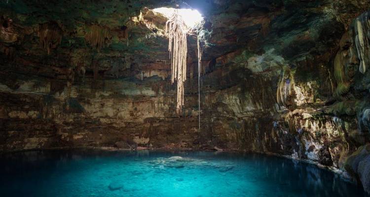 Cénote souterrain avec une eau turquoise illuminée par un rayon de lumière du jour provenant d'une ouverture au-dessus