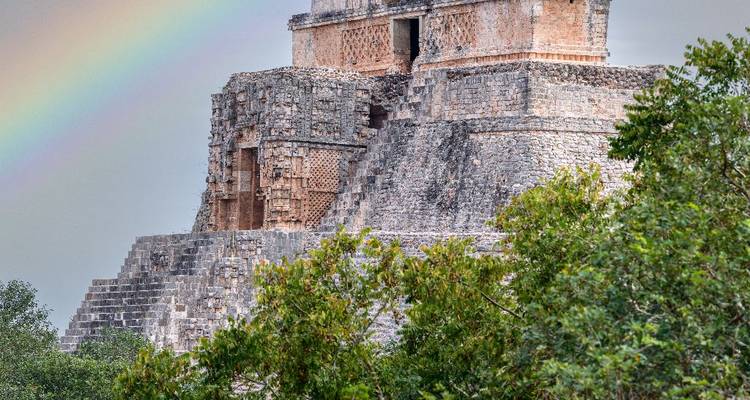 Temple maya d'Uxmal avec maçonnerie encadrée de verdure et un arc-en-ciel s'arquant au-dessus