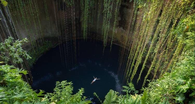 Voyageur flottant paisiblement dans un cénote bleu profond drapé de lianes vertes suspendues