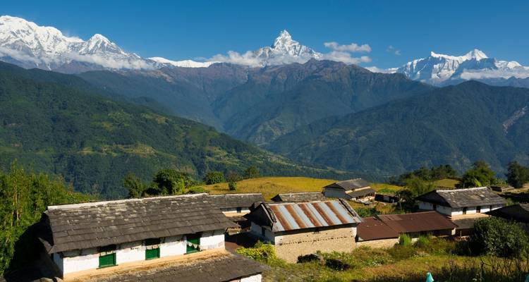Cottages en pierre sur des terres agricoles vallonnées face à une majestueuse ligne de sommets himalayens sous un ciel dégagé