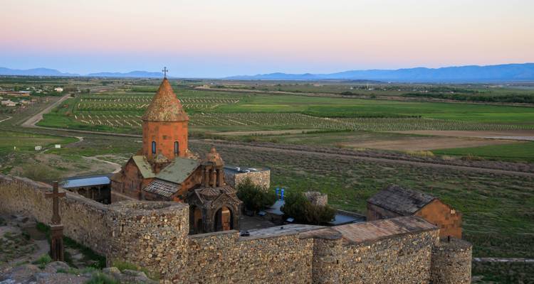 Monastère historique de Khor Virap et murs fortifiés surplombant de vastes plaines vertes à l'aube avec un ciel pastel