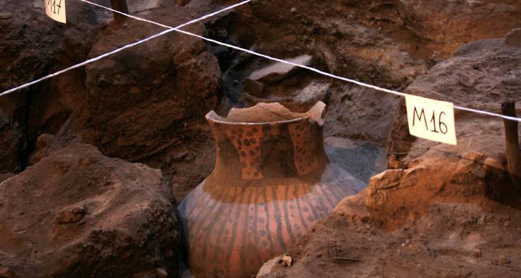 Fosse de terre excavée révélant un pot en céramique ancien décoré sur un site de fouilles archéologiques