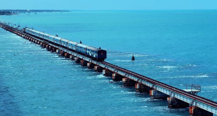 Un train bleu traverse le long pont ferroviaire de Pamban au-dessus des eaux marines d'un bleu vibrant.