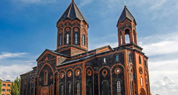 Catedral de piedra negra y naranja impresionante con torres gemelas bajo un cielo azul brillante.