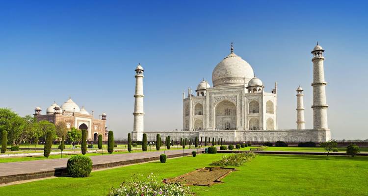 De witmarmeren Taj Mahal omlijst door blauwe lucht en weelderige groene gazons.