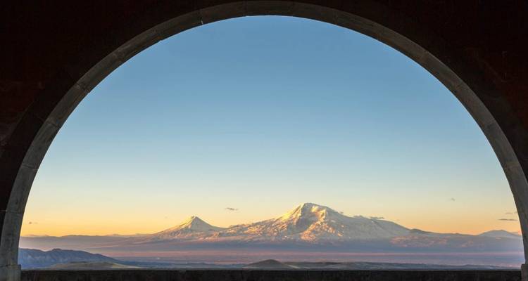 Macizo del Ararat nevado brillando con la luz del amanecer visto a través de un arco de piedra.