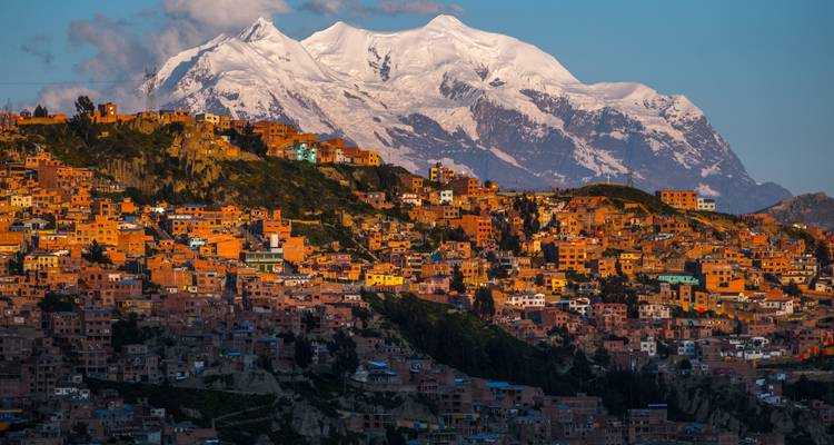 La Paz's bakstenen huizen dalen trapsgewijs af langs hellingen onder de besneeuwde Illimani tijdens het gouden uur.