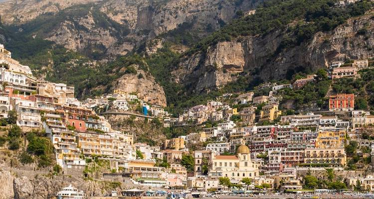 Vista amplia de los edificios de colores pastel de Positano y la iglesia con cúpula enclavados contra espectaculares acantilados sobre el Mediterráneo.