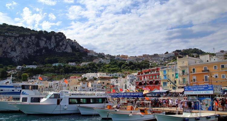Puerto bullicioso en Capri con transbordadores, pequeñas embarcaciones y vibrantes edificios costeros respaldados por una ladera rocosa.