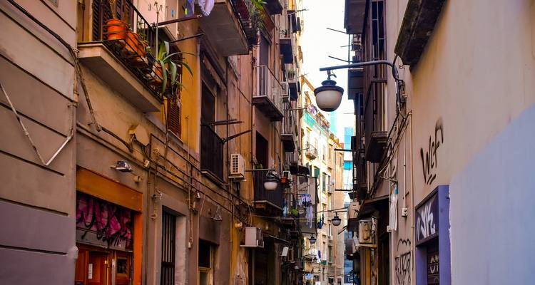 Callejón italiano estrecho bordeado de balcones, farolas y fachadas urbanas coloridas.