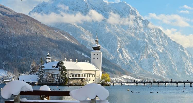 Schneebedecktes Schloss Ort am Traunsee vor der Kulisse hoch aufragender Winterberge.