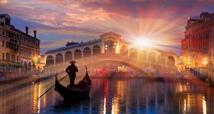 Gondolero silueteado en canal tranquilo con el Puente de Rialto y dramático resplandor solar al atardecer en Venecia.