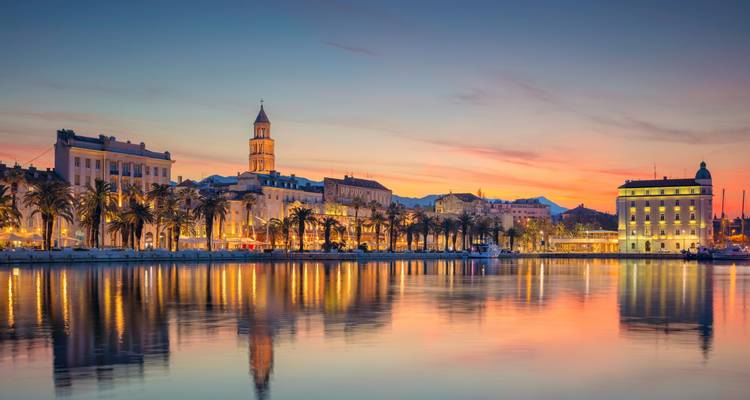 Atardecer sobre el paseo marítimo de Split con el paseo Riva bordeado de palmeras y el campanario reflejándose en las tranquilas aguas del Adriático.