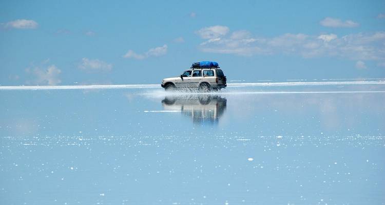 Un véhicule 4x4 glisse sur la surface réfléchissante comme un miroir du Salar d'Uyuni inondé.